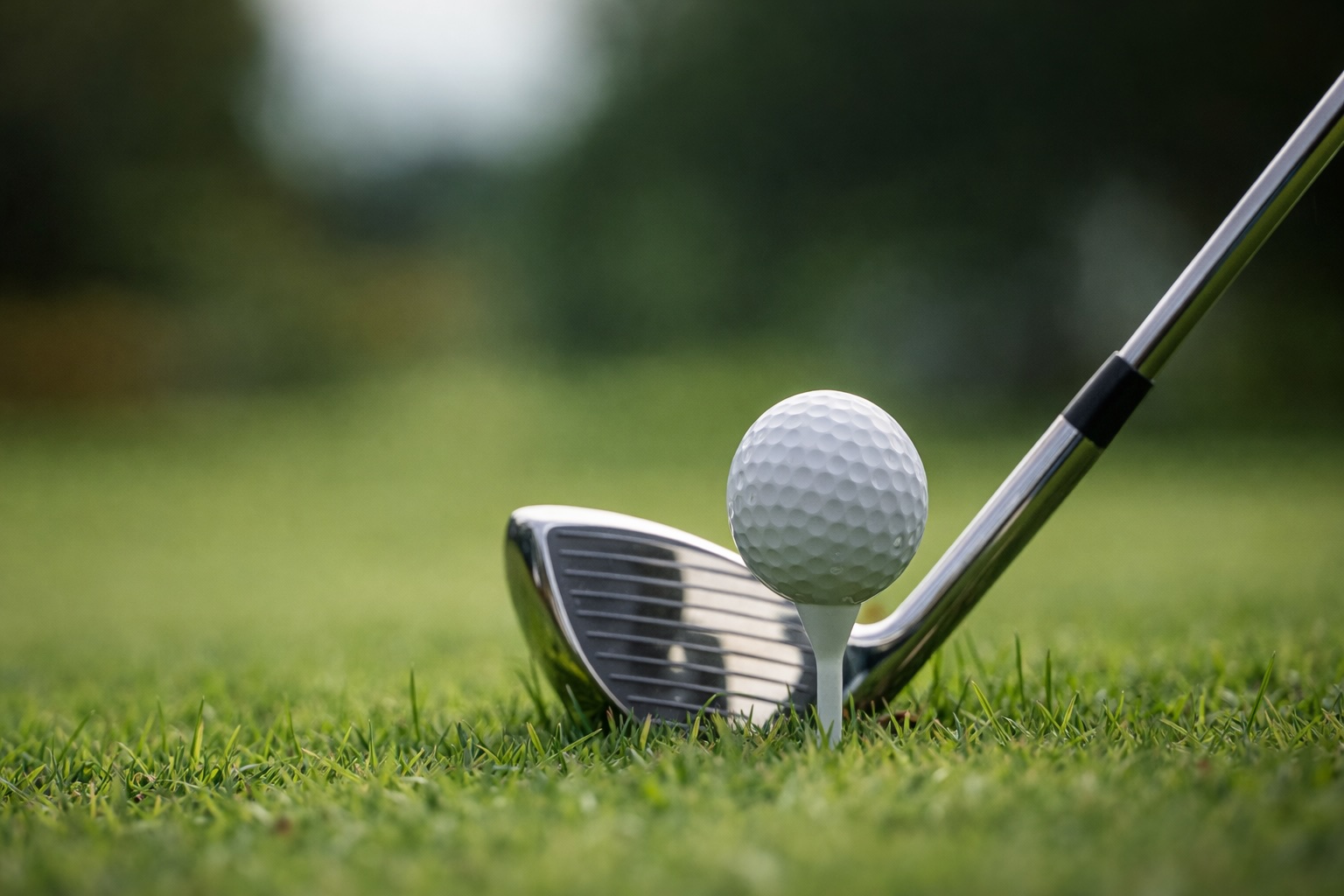 Golf ball on tee with iron club on green grass